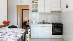 A kitchen with white cabinets, a stove, a sink, and a small shelf with kitchenware.
