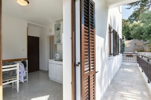 A corridor with a white wall, a wooden door, and a window with shutters.