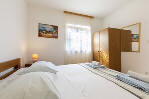 Une chambre d’hôtel avec un lit, une table de chevet avec une lampe, une fenêtre avec des rideaux, une armoire et un tableau au mur.