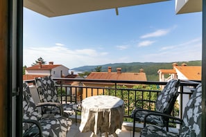 A balcony with outdoor furniture, a table, and a view of a mountainous landscape.
