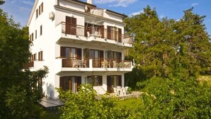 A two-story white building with balconies, surrounded by greenery.