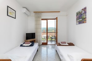 A hotel room with two beds, a TV, a balcony with a table and chairs, and a painting on the wall.