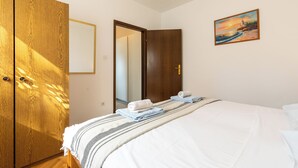 A bedroom with a bed, a wooden wardrobe, a painting, and a door leading to another room.