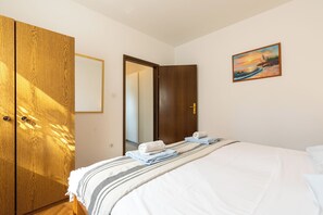 Une chambre à coucher avec un lit, une armoire en bois, un tableau et une porte donnant sur une autre pièce.