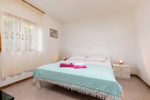 Un dormitorio ordenado con cama, mesitas de noche y ventana con cortinas.