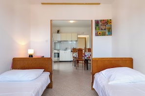 Habitación de hotel con dos camas, una mesa de comedor y una cocina al fondo.