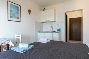 Une chambre avec un lit, un petit coin cuisine, une chaise blanche et une porte.