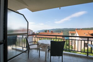 A balcony with a table and chairs, a view of the sea and mountains, and a clear sky.