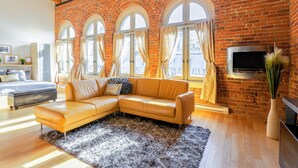 A modern living room with a brick wall, large windows, a leather sofa, and a flat-screen TV. - Authentic loft for family of 4 in the heart of Old Quebec (La Cité-Limoilou)