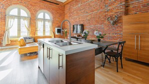 A kitchen with a brick wall, wooden cabinets, a sink, and a dining area with a table and chairs. - Authentic loft for family of 4 in the heart of Old Quebec (La Cité-Limoilou)