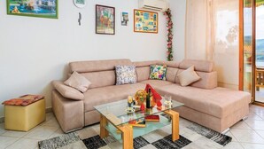 A living room with a beige sofa, a glass coffee table, and a small side table. There are framed pictures on the wall, an air conditioning unit, and a window with a view. - Apartment 832/1950 (Istria - Rabac), 700m from the beach (Rabac)
