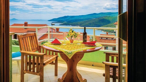 A balcony with a table set for two, a wooden chair, and a view of the sea and hills. - Apartment 832/1950 (Istria - Rabac), 700m from the beach (Rabac)
