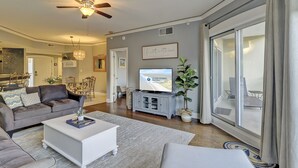 A modern living room with a ceiling fan, a flat-screen TV, a dining area, and a large sliding glass door to the outdoors. - Ocean Views in Palmetto Dunes- Great amenities! (Hilton Head)