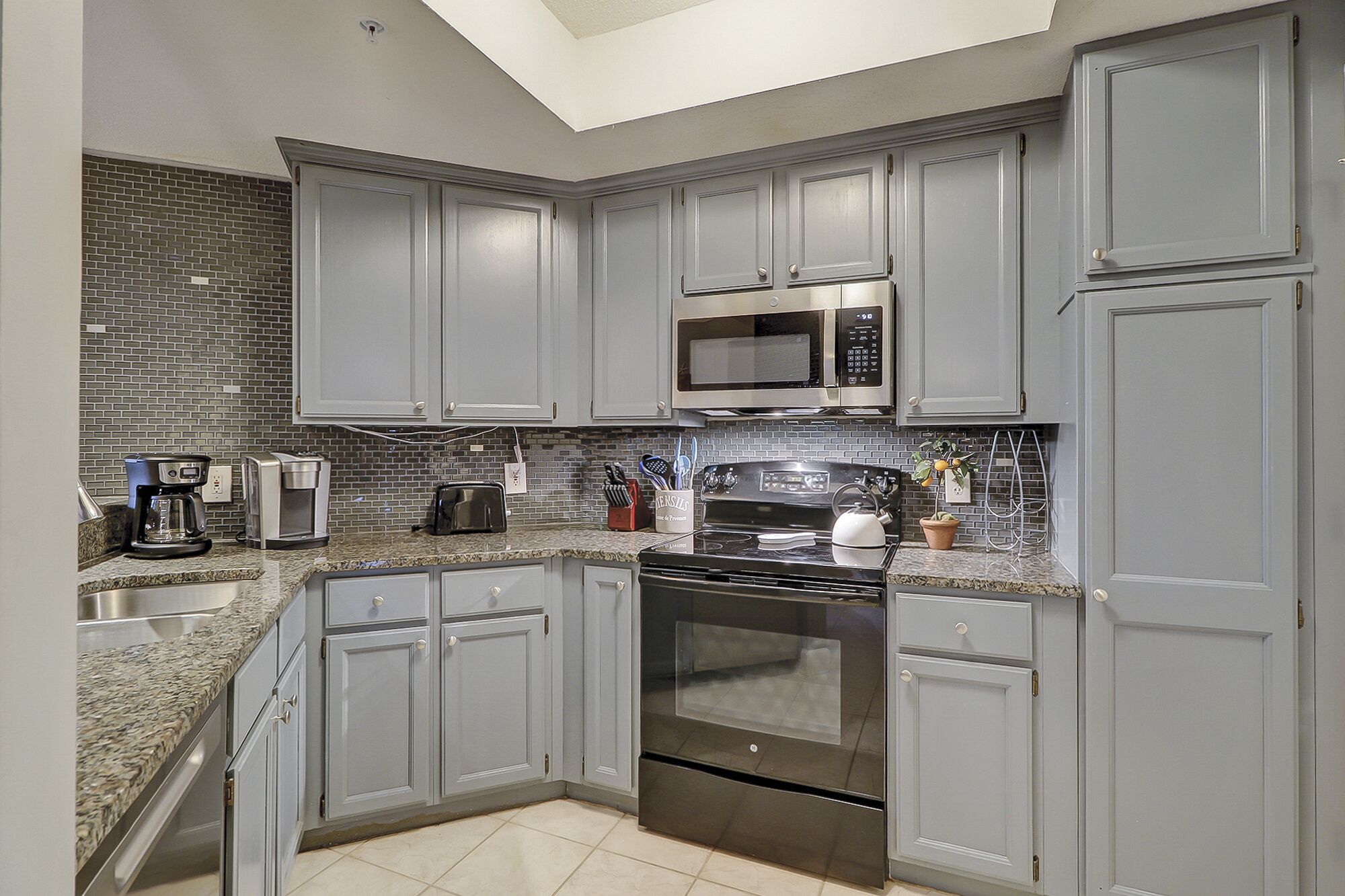 A modern kitchen with grey cabinets, a stainless steel microwave, a stove, and a coffee maker.