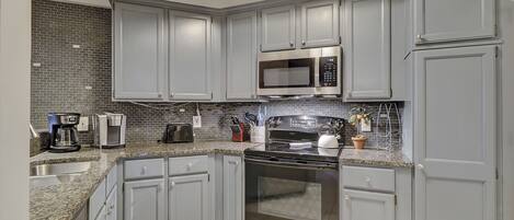 A modern kitchen with grey cabinets, a stainless steel microwave, a stove, and a coffee maker.