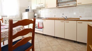 A compact kitchen with white cabinets, a wooden chair, and a tiled backsplash.