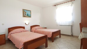 A bedroom with two wooden beds, a nightstand, a radiator, and a window with curtains.