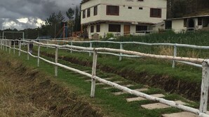A two-story building with a white exterior and red window frames, surrounded by a grassy area and a wooden fence. - Finca El Yagual (Olmedo)