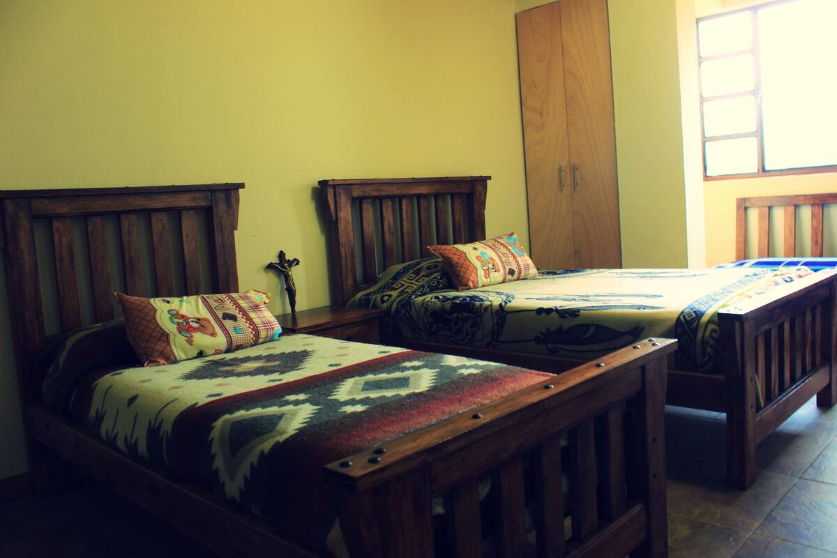 Two wooden beds with patterned bedding, a wooden wardrobe, and a window with a view.