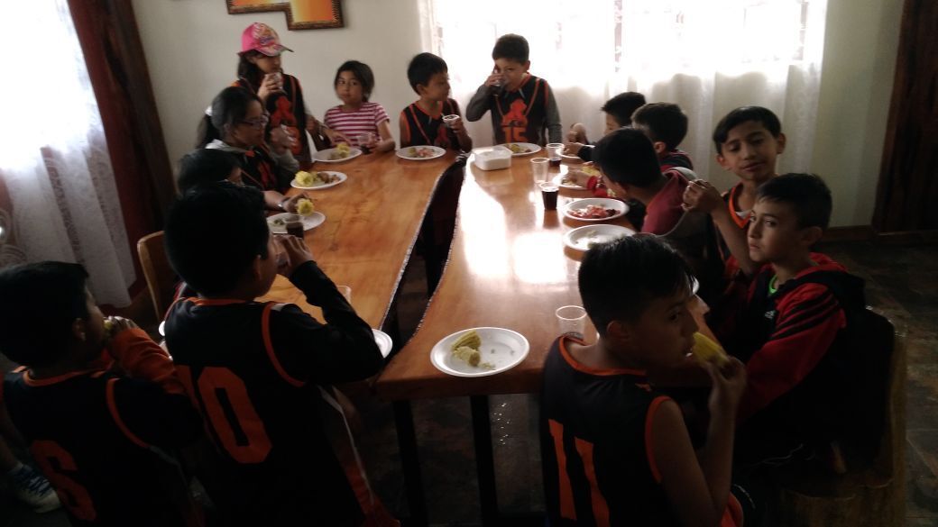 A group of children sitting around a long wooden table, eating.