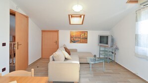 A small, well-lit room with a sofa, a television, and a painting of a canal scene.