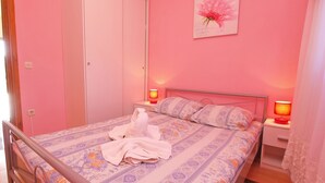 Un dormitorio con decoración rosa, una cama, dos lámparas de noche, una mesita de noche y una puerta.