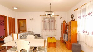 Una sala de estar con una mesa de comedor, sillas, un sofá, un televisor y una estantería.