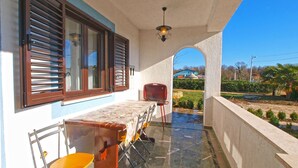 Un área de estar techada al aire libre con una mesa y sillas, vistas del paisaje circundante y un edificio al fondo.