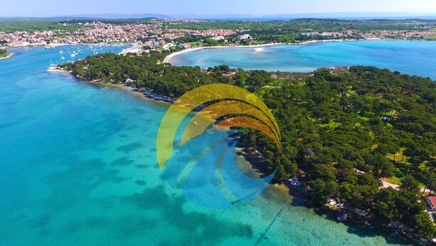 Une vue aérienne d’une zone côtière, avec des eaux turquoise limpides, une petite île couverte d’une végétation luxuriante et, au loin, une ville avec ses bâtiments et son littoral.