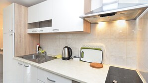 Une cuisine moderne avec des meubles blancs, un évier en acier inoxydable, une bouilloire, un grille-pain et un four encastré.