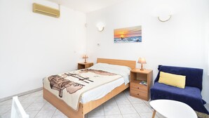 Une chambre à coucher comprenant un lit, des tables de chevet, un canapé, une petite table, un climatiseur fixé au mur, une lampe fixée au mur et un tableau.