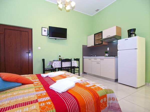 A small, well-lit bedroom with a bed, a bedside table, and a television mounted on the wall.