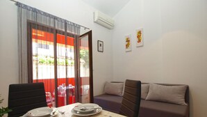 A dining area with a table set for two, a sofa, and a sliding glass door leading to an outdoor area.