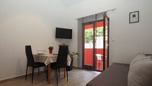 A room with a dining table, chairs, a TV, a sofa, and a sliding glass door leading to an outdoor area.