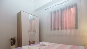 A bedroom with a bed, a wardrobe, a window with sheer curtains, and a vase with dried flowers.