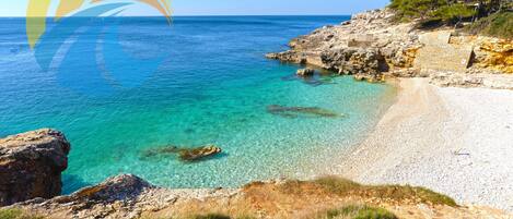 A coastal landscape with clear turquoise waters, rocky cliffs, and a sandy beach.