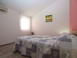 Una camera da letto con un letto, una finestra con tende leggere, un condizionatore d'aria a parete e un quadro.
