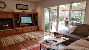 Een woonkamer met een open haard, televisie, bank en uitzicht op de omgeving door grote schuifdeuren.