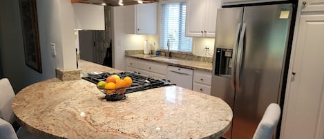 Cozinha moderna com ilha de granito, eletrodomésticos de aço inoxidável e cadeiras cinza claro.