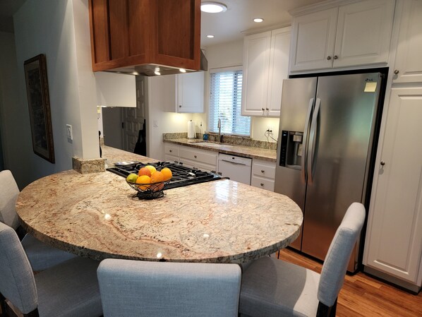 Una cocina moderna con una isla de granito, electrodomésticos de acero inoxidable y sillas de color gris claro.