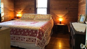 A wooden cabin bedroom with a bed, two bedside lamps, a window, and a dresser with a mirror.