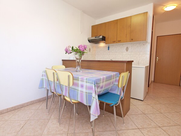 A small kitchen with a tiled floor, a table with a plaid tablecloth, four chairs, and a refrigerator. - Apartment 909/2115 (Istria - Valbandon), 700m from the beach (Valbandon)