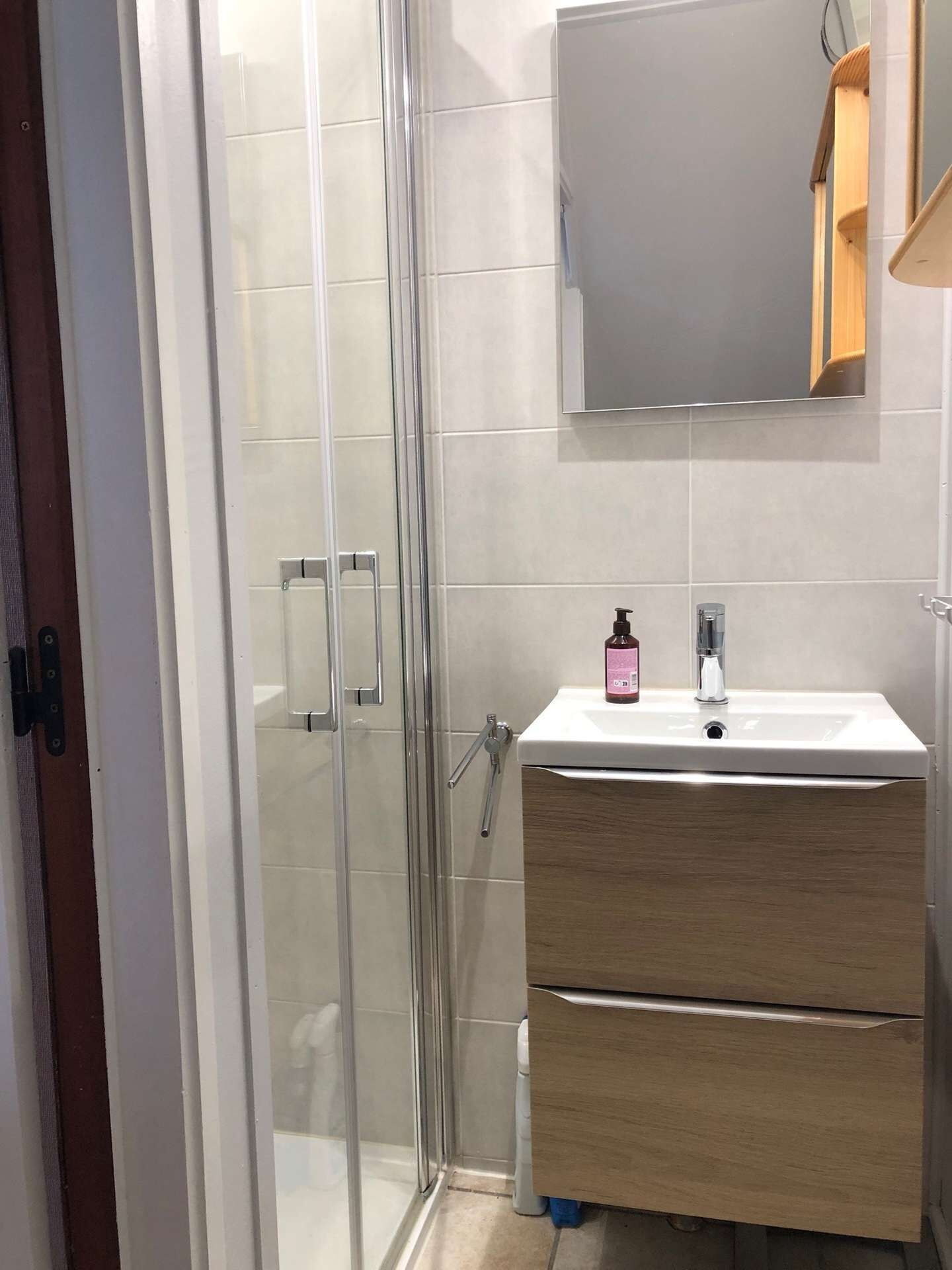 A modern bathroom with a glass shower enclosure, a white sink with a wooden vanity, and a mirror above the sink.