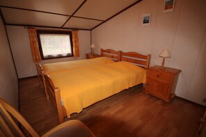 Een slaapkamer met een houten bed, twee nachtkastjes met lampen, een houten stoel en een raam met gordijnen.