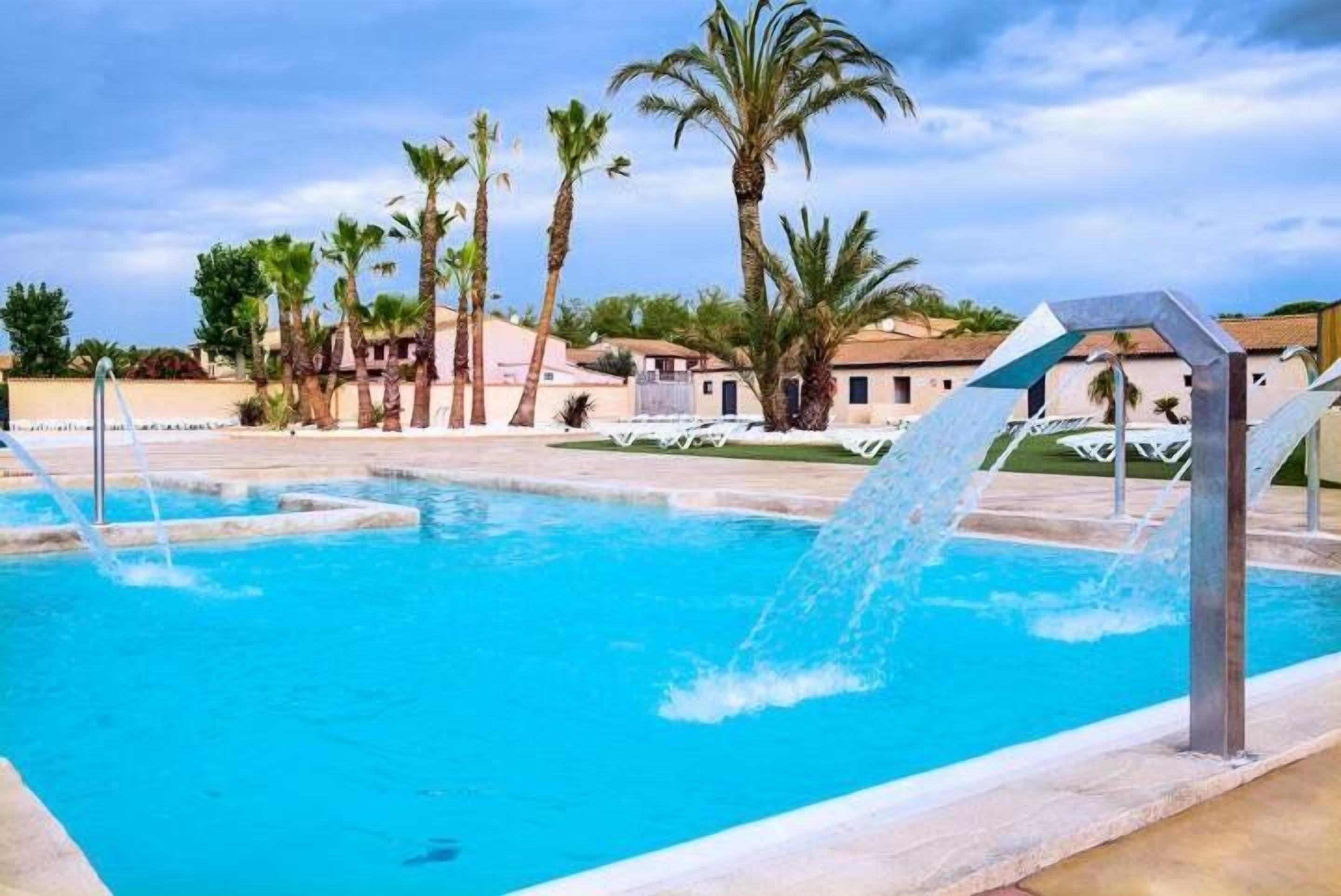 A swimming pool with water features, surrounded by palm trees and buildings.