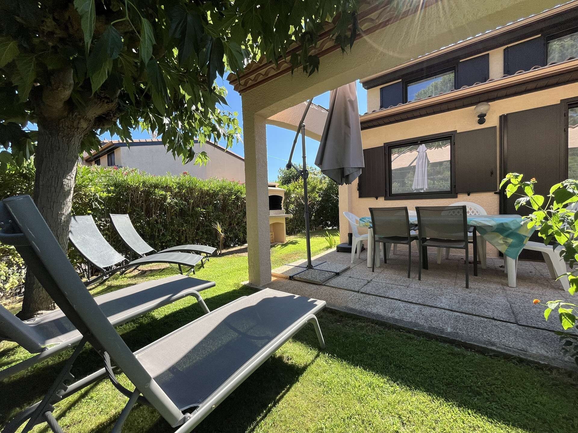 A patio area with outdoor furniture, including lounge chairs and a table, under a pergola.