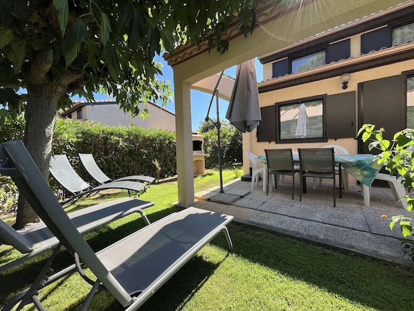 A patio area with outdoor furniture, including lounge chairs and a table, under a pergola.