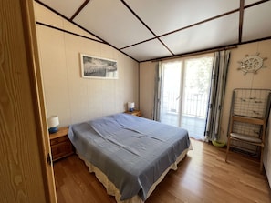 A bedroom with a bed, a nightstand, a window with curtains, a wall-mounted ship's wheel decoration, and a wooden floor.