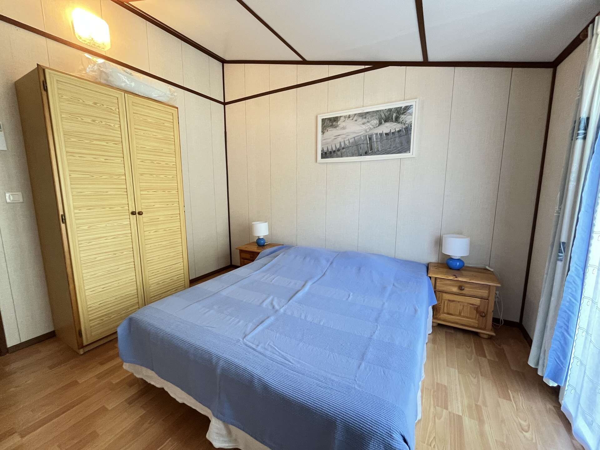 Een slaapkamer met een bed, een houten kledingkast, nachtkastjes en een ingelijst beeld aan de wand.