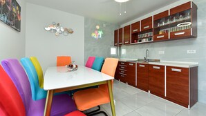 A modern kitchen with wooden cabinets, a white countertop, and a dining area with colorful chairs.